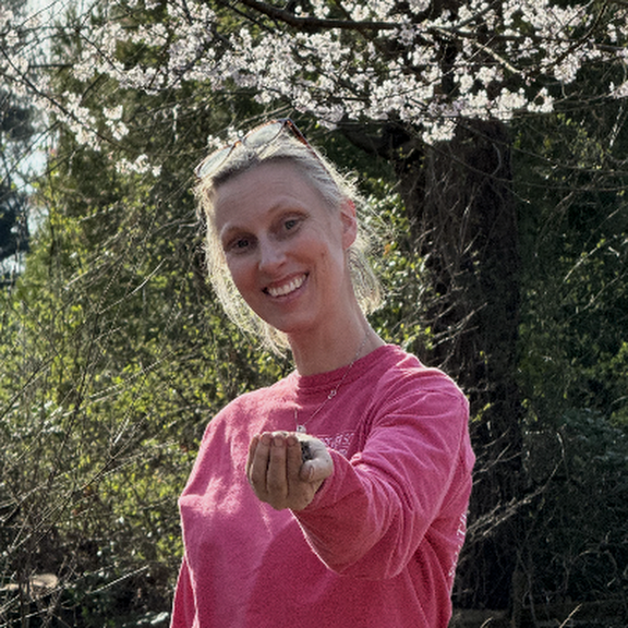 Jen holding freshly harvested garlic outdoors beneath spring blossoms.